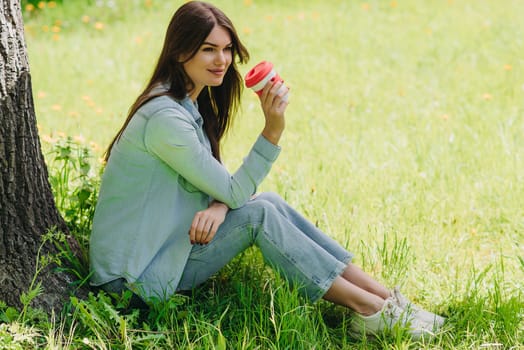 Beautiful girl enjoying a cup of coffee sitting under tree in park