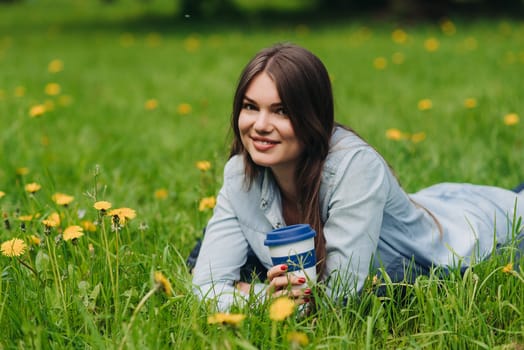 Beautiful young woman laying on the grass with cup of takeaway drink