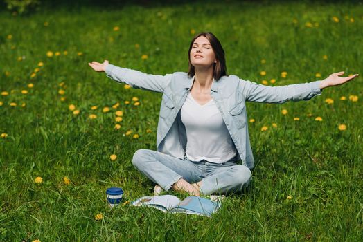 Beautiful young woman enjoy nature sitting in park with book and coffee