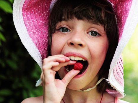 Beautiful girl in a hat eating raspberries on nature.