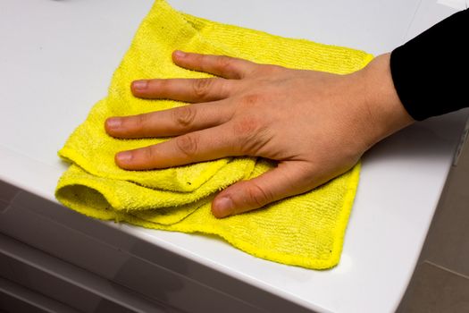 person is cleaning wash mashine with the yellow rag in bathroom