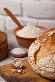 Crannied rustical homemade white bread on old cutting board with a pile of fresh yeast and cooking ingredients.