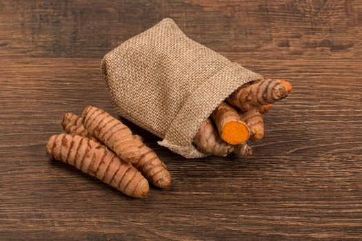 Raw turmeric root in burlap sack on wooden surface