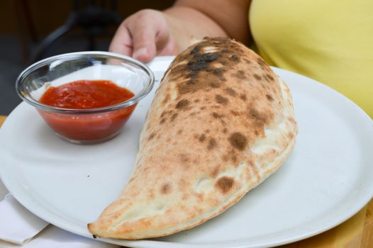 Pizza calzone served on a white plate with tomato puree in
Glass bowl