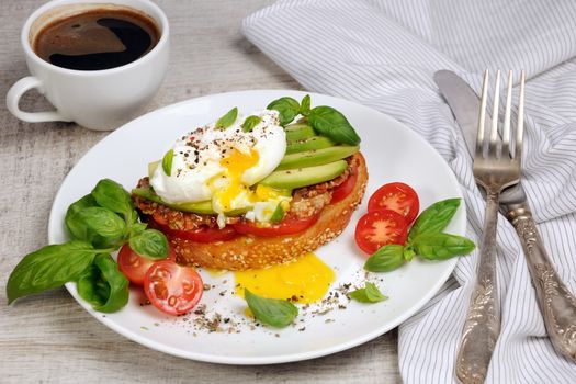 Egg poached on a toasted slice of baguette with tomato, spicy ham and avocado, sprinkled   spices and basil