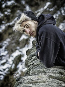 Portrait of young man in hoodie posing outdoor in winter setting with snow all around, looking at camera.