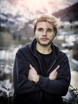 Portrait of young man in hoodie posing outdoor in winter setting with snow all around, looking at camera.