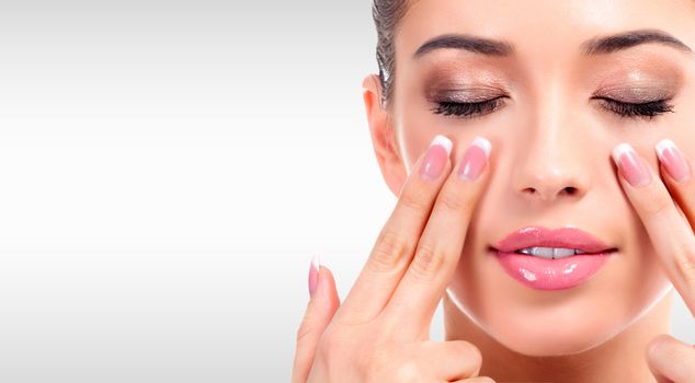 Closeup shot of young beauty woman massaging her face. Facial massage concept. Pretty girl against a grey background with copyspace