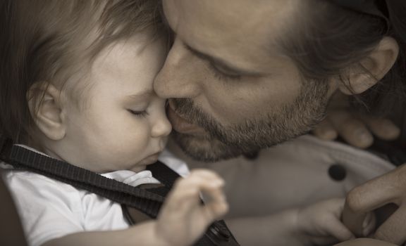 A father is kissing gently his young baby boy on the nose. Aged photo effect.
