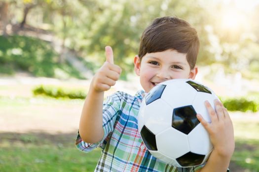 Cute Young Boy Playing with Soccer Ball and Thumbs Up Outdoors in the Park.
