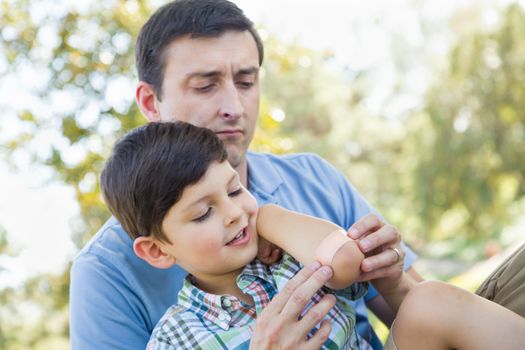 Loving Father Puts a Bandage on the Elbow of His Young Son in the Park.