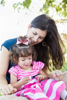 Mixed Race Young Mother and Cute Baby Girl Applying Fingernail Polish in the Park.