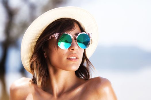 portrait of a sexy girl posing with sunglasses and a hat on a beach