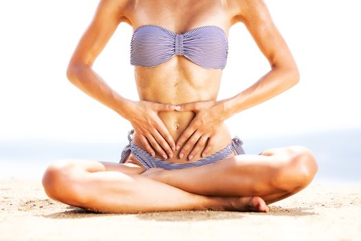 sexy female body on a beach, touching her belly with sand