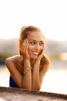 beautiful girl on an upturned rowboat smiling and enjoying a sunset