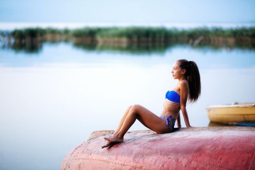 beautiful girl on a rowboat, sunset time on a lake. full body shot