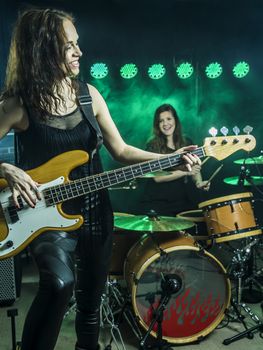 Photo of a female bass player and drummer of a rock band playing on stage.