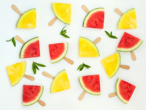 Red and yellow watermelon slices on wooden sticks with mint leaves among them on a white background. Flat lay, top view, copy space