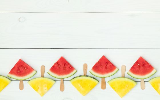 Red and yellow watermelon slices on wooden sticks on a white wooden background. Flat lay, top view, copy space