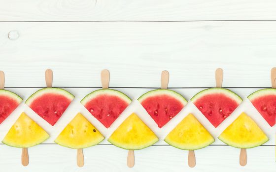 Red and yellow watermelon slices on wooden sticks on a white wooden background. Flat lay, top view, copy space