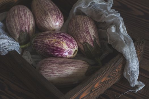 Purple graffiti eggplants in a wooden box in a vintage wooden background in rustic style, selective focus. Toned