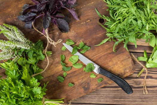 Fresh organic green herbs wooden floor with copy space. Green and violet plants background. Healthy eating background. Vegetarian food, organic food.