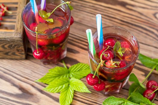 Glasses of refreshing  drink flavored with fresh fruit and decorated with cherries covered with dew drops. Wooden background