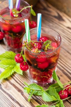 Glasses of refreshing  drink flavored with fresh fruit and decorated with cherries covered with dew drops. Wooden background