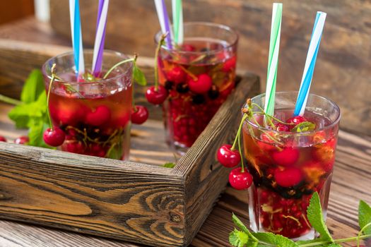 Three glasses of refreshing  drink flavored with fresh fruit in wooden box surrounded by fruit. Wooden background