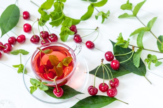 Fresh fruit cherry drink in transparent glass cup surrounded by cherries on the white wooden background. Top view