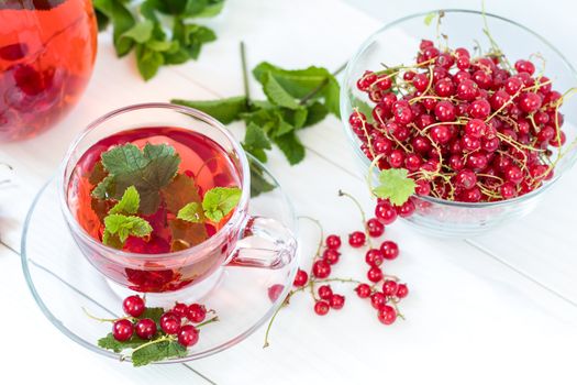 Redcurrant drink in transparent glass carafe and cup. Clear glass vase with red currant berries on the white wooden background