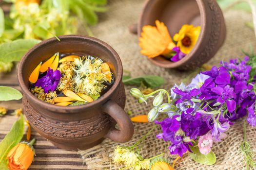 Two ceramic cups of healthy herbal tea with decoction of dry and fresh flowers on dark aged rustic wooden background. Shallow depth of field.