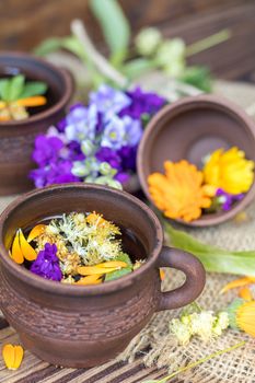 Two ceramic cups of healthy herbal tea with decoction of dry and fresh flowers on dark aged rustic wooden background. Shallow depth of field.