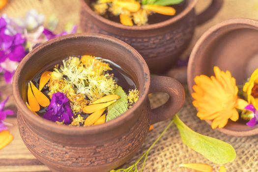 Two ceramic cups of healthy herbal tea with decoction of dry and fresh flowers on dark aged rustic wooden background. Shallow depth of field.