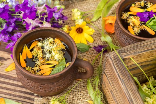 Two ceramic cups of healthy herbal tea with decoction of dry and fresh flowers on dark aged rustic wooden background. Shallow depth of field.