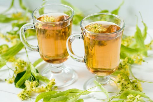 Linden flower tea in a transparent grog glass with a linden blossom on the white wooden surface