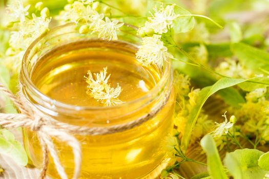 Honey in glass jars with white linden flowers on light wooden background. Shallow depth of field.