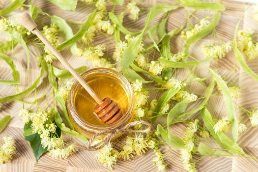 Honey in glass jars with white linden flowers on light wooden background. Shallow depth of field.