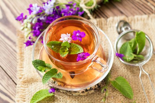 Glass cup of summer herbal tea with fresh mint and field larkspur. Wooden table. Shallow depth of field.