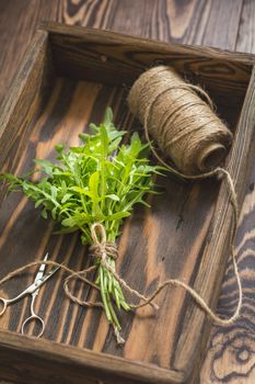 Top view of the bunch of fresh arugula in a wooden box. Dark wooden background. Toned photo. Shallow depth of the field.