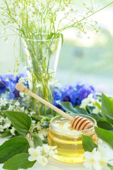 Honey in glass jars with jasmine flowers on windowsill. Shallow depth of field.