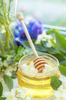 Honey in glass jars with jasmine flowers on windowsill. Shallow depth of field.