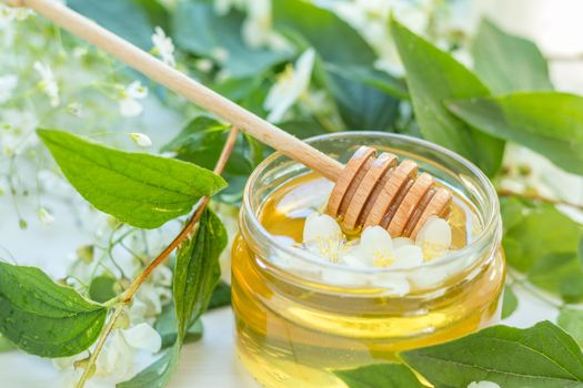 Honey in glass jars with jasmine flowers on windowsill. Shallow depth of field.