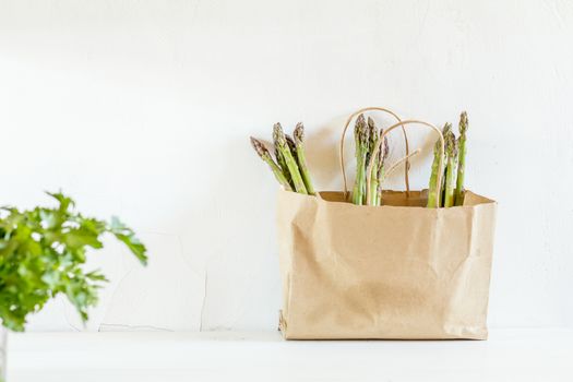 Bunches of fresh asparagus in a paper bag on white cracked wallbackground. Copy space