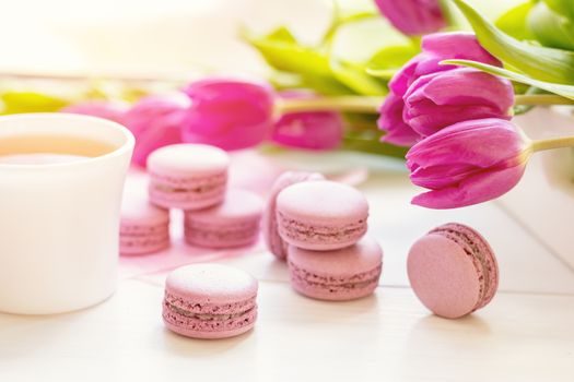 Violet sweet delicious macaroons and fresh tulips on white background. Cup of hot tea. Shallow depth of field. Coloring toned photo.