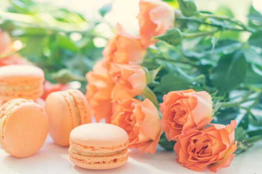Orange mango or citrous macaroons and orange fresh little roses on light wooden background. Coloring and processing photo with light vintage style. Toned. Shallow depth of field.