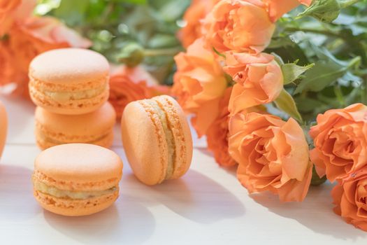 Orange mango or citrous macaroons and orange fresh little roses on light wooden background. Coloring and processing photo with light vintage style. Toned. Shallow depth of field.