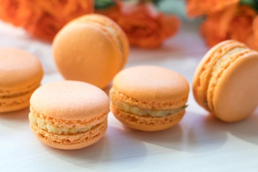 Orange mango or citrous macaroons and orange fresh little roses on light wooden background. Coloring and processing photo with light vintage style. Toned. Shallow depth of field.