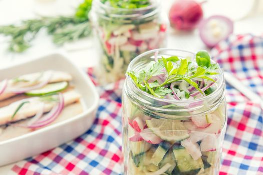 Homemade healthy salads with vegetables, onion, parsley and lettuce in jar. Sliced herring fillets, cut onion and lime on white plate. Toning. Selective focus.