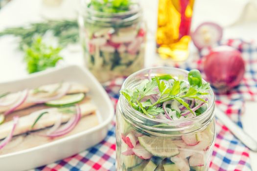 Homemade healthy salads with vegetables, onion, parsley and lettuce in jar. Sliced herring fillets, cut onion and lime on white plate. Toning. Selective focus.